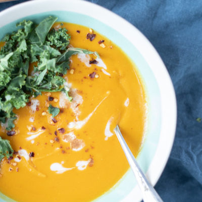 overhead shot of sweet potato carrot soup in a bowl with swirls of coconut milk and topped with kale