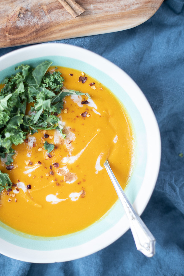 overhead shot of sweet potato carrot soup in a bowl with swirls of coconut milk and topped with kale