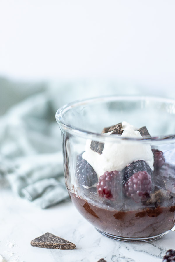 side view of a brownie mug cake topped with blackberries and whipped cream in a glass mug