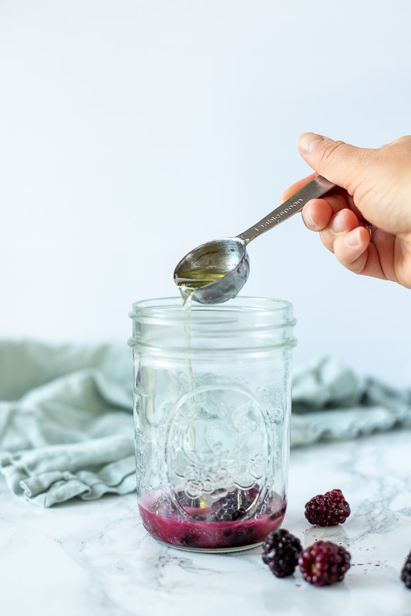 adding wet ingredients to blackberries in a mason jar