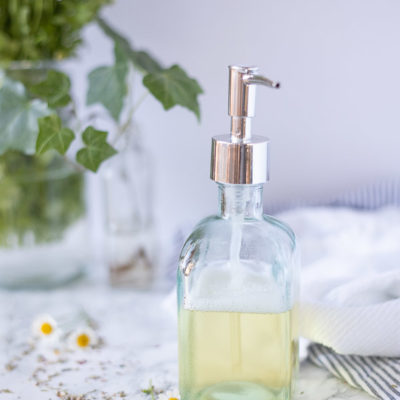 homemade body wash in a soup dispenser with dried flowers around the dispenser and fresh chamomile in the background