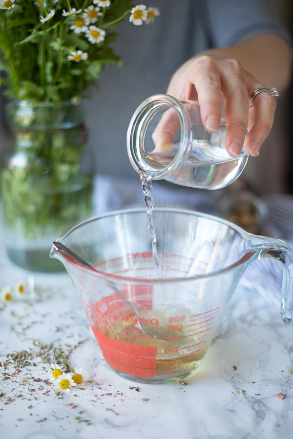 water being poured into a glass measuring cup with Castile soap in it