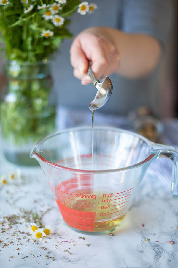 vegetable glycerin in a antique measuring spoon being poured into a measuring cup of Castile soap and water