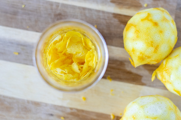 overheard shot of lemon peels in a mason jar with vodka poured over. Lemon are placed to the right