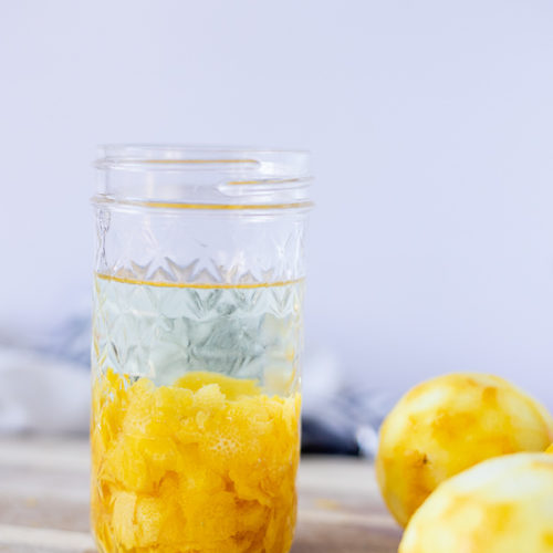 homemade lemon extract in a mason jar on top a wood cutting board with lemons around