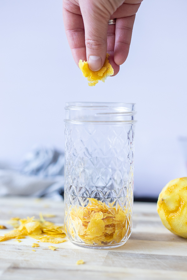 hand adding lemon peels to a glass mason jar