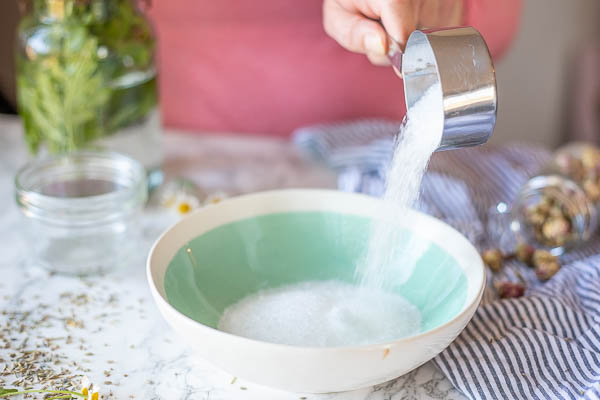 adding Epsom salts to a a teal bowl with baking soda in it