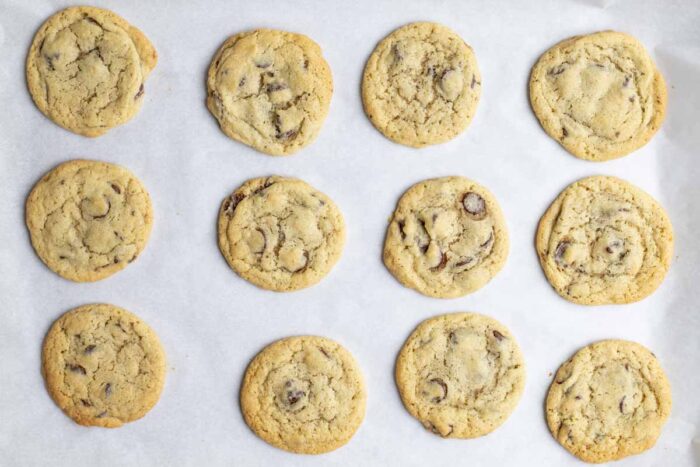 A parchment lined pan of fresh baked sourdough chocolate chip cookies.