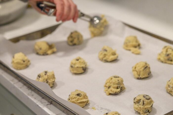 Sourdough chocolate chip cookie dough being scooped onto a parchment lined baking sheet.