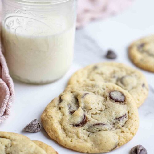 Sourdough chocolate chip cookies on a marble countertop with a glass of milk and a pink towel in the background.