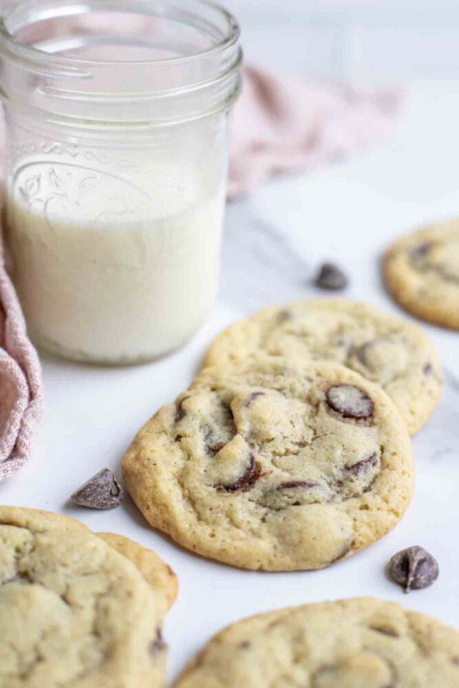 Sourdough chocolate chip cookies on a marble countertop with a glass of milk and a pink towel in the background.