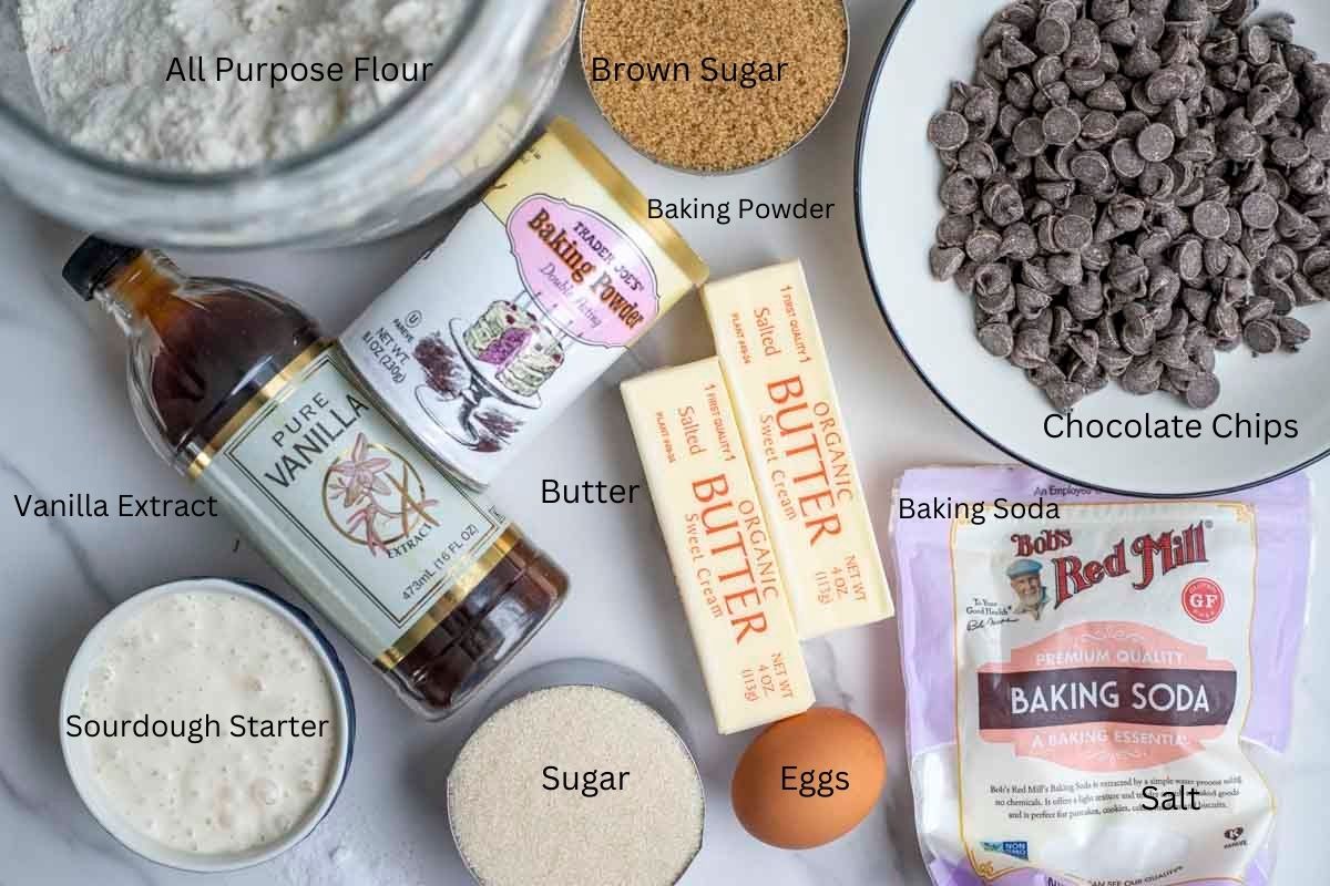 Flour, chocolate chips, butter, sugar, and more ingredients on a marble countertop.