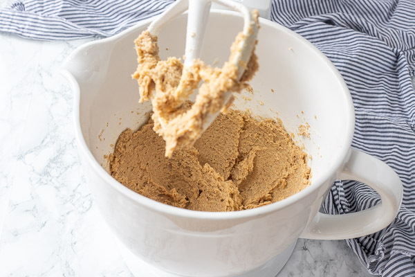 butter, sugar, and brown sugar creamed together in a white ceramic mixing bowl on a stand mixer