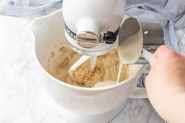sourdough starter, eggs, and vanilla being added to creamed sugar in a white ceramic mixing bowl on a stand mixer