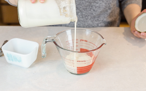 pouring sourdough starter discard into a measuring cup that is sitting on a concrete countertop