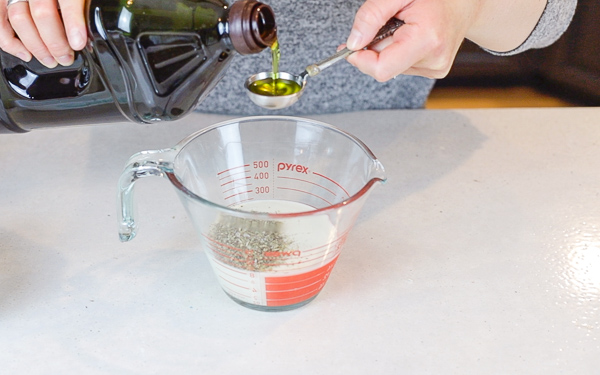 measuring olive oil into a measuring cup with sourdough starter and seasoning to make sourdough crackers