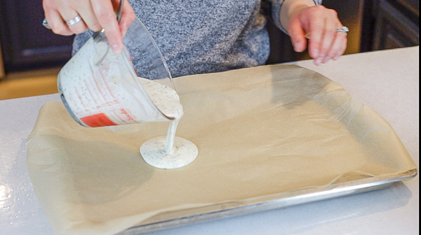 pouring homemade cracker batter onto a parchment lined baking sheet