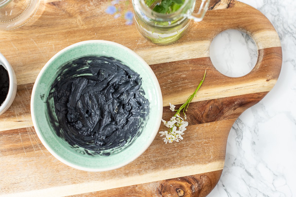 diy armpit detox mask in a cream and teal bowl on a wood cutting board with fresh flowers