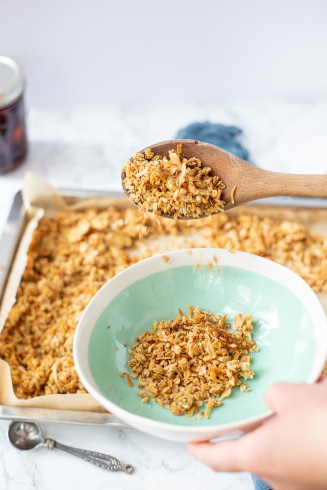 coconut granola being scooped out with a wooden spoon from a pan to a bowl
