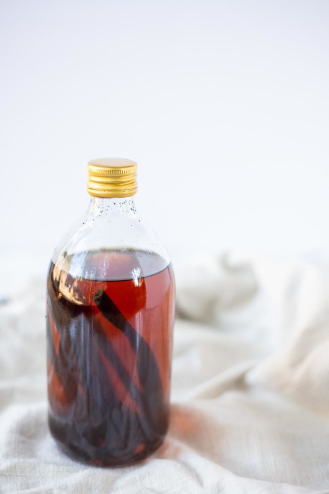 homemade vanilla extract in a glass bottle with a gold lid on a cream colored towel