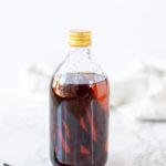 homemade vanilla extract in a glass bottle with a vanilla bean to the left and a cream towel in the background