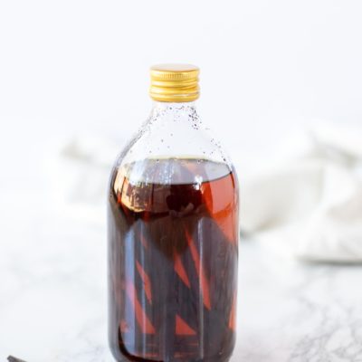 homemade vanilla extract in a glass bottle with a vanilla bean to the left and a cream towel in the background