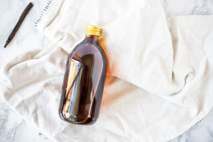homemade vanilla extract in a glass bottle with a gold lid laying on a tan towel