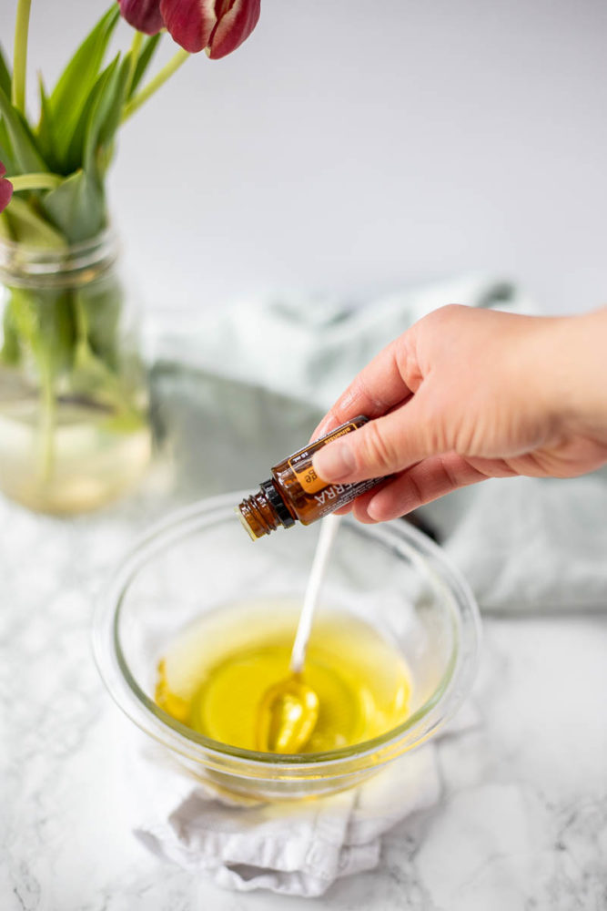 adding essential oils to melted oil and shea butter in a glass bowl