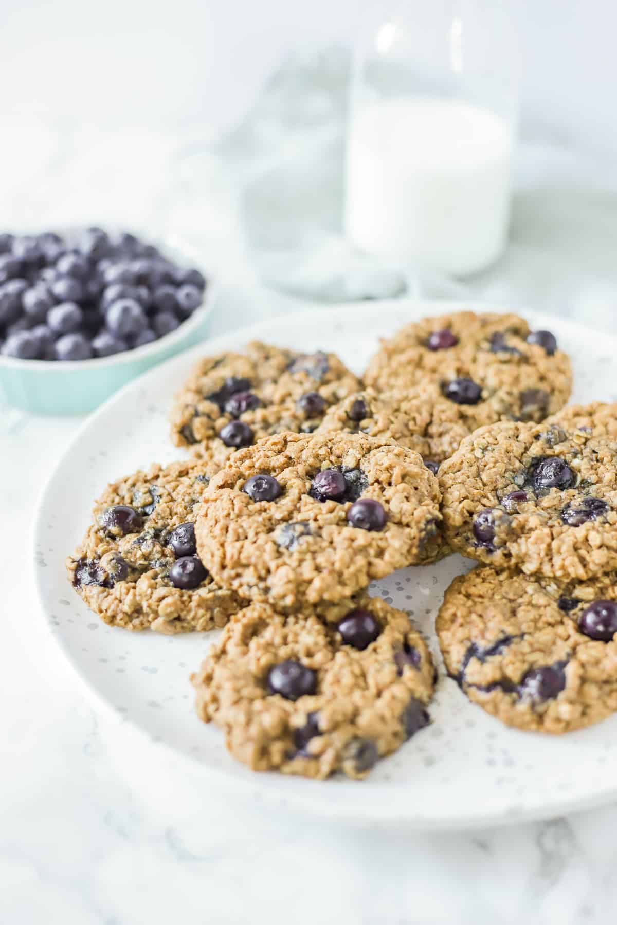 blueberry oatmeal cookies on a blue and white plate with blueberries and milk in the background