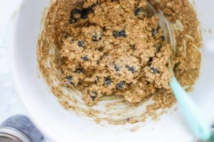 blueberries folded into oatmeal cookie batter in a stand mixer with a turquoise silicon spoon in the bowl