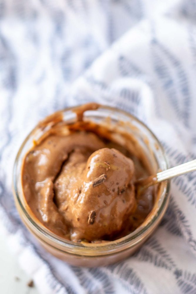 bowl of chocolate peanut butter banana ice cream in a glass jar on top of a white and blue napkin