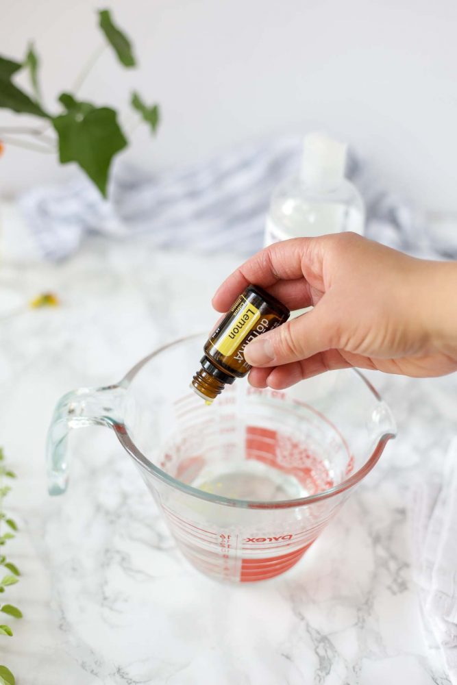 adding lemon essential oils to a homemade dish soap in a glass measuring cup