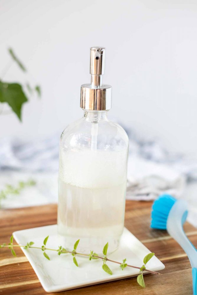 diy dish soap in a glass soap pump jar on a white plate with oregano on a white plate