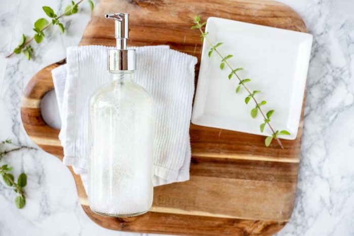 natural soap in a glass jar on a white dish cloth on a wood cutting board with a white plate to the right