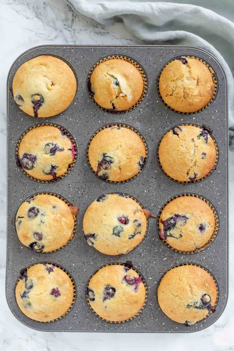 muffin pan of sourdough blueberry muffins on a marble countertop with a napkin to the top right
