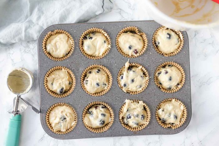 sourdough blueberry muffin batter in a lined muffin tin with an ice cream scooper to the left