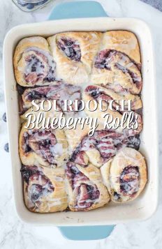 blueberry sourdough sweet rolls topped with icing in a blue and cream baking dish