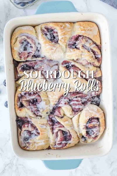 blueberry sourdough sweet rolls topped with icing in a blue and cream baking dish