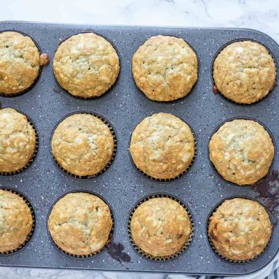 sourdough banana muffins in a muffin tin on a cream and blue stripped towel