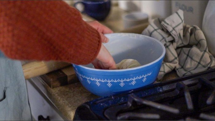women kneading sourdough raspberry roll dough in a antique blue bowl in her kitchen