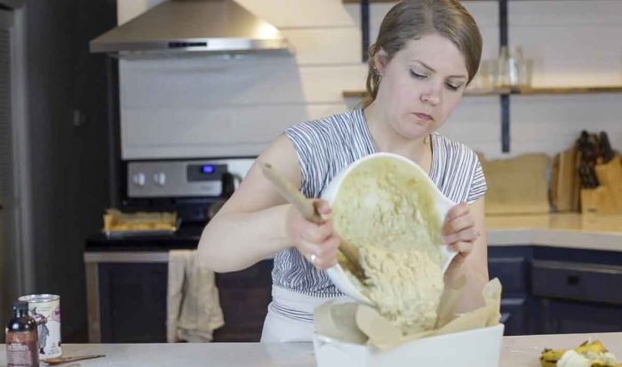 woman wearing a blue and white stripped shirt pouring sourdough banana bread batter into a parchment lined loaf pan