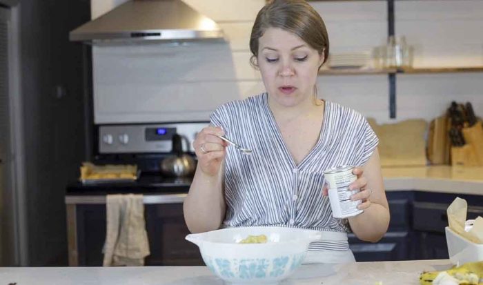 woman wearing a blue stripped shirt adding baking powder to a antique bowl