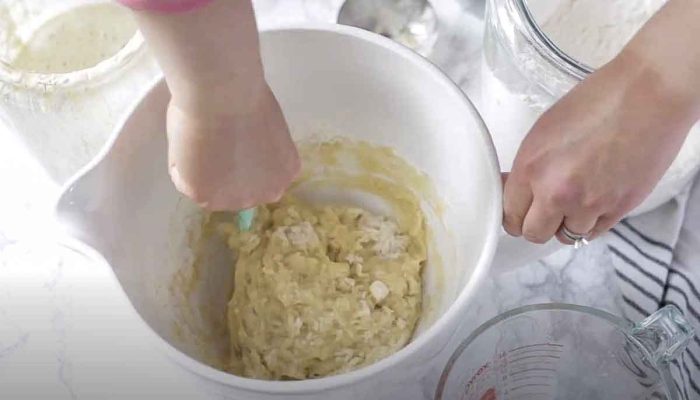 hand mixing together sourdough starter, flour, honey, and melted butter in a white stand mixer bowl