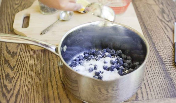 sugar being added to fresh blueberries in a saucepan 