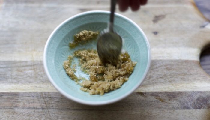 mixing diy lip scrub in a teal bowl on a wood cutting board