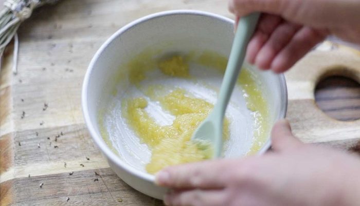 teal silicon spoon mixing together diy scalp scrub in a cream bowl on a wooden cutting board