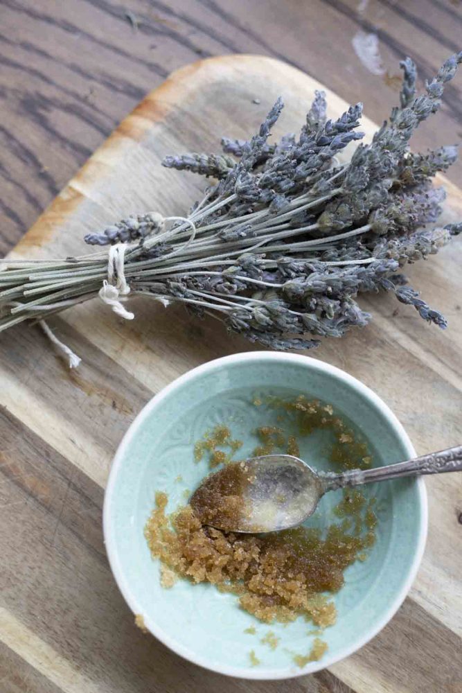 lip scrub in a teal bowl on a wood cutting board with a bundle of lavender