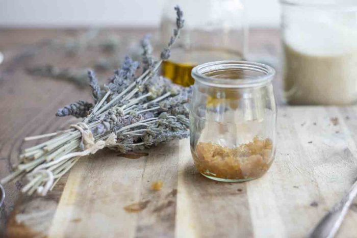 jar of brown sugar lip scrub on a wood cutting board with dried lavender and two jars of sugar and oil in the background