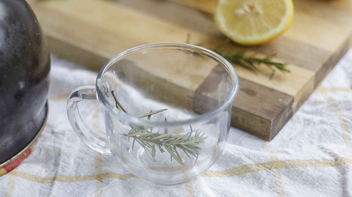 fresh sprigs of rosemary in a glass mug with a cutting board with sliced lemons in the background