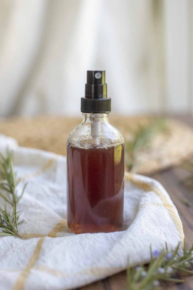 a bottle of rosemary water for hair on a white and yellow towel with fresh sprigs of rosemary surrounding the towel
